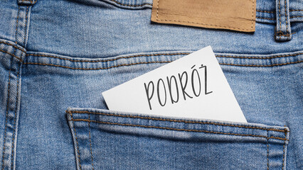 White card with a handwritten inscription "Podr&oacute;ż", inserted into the pocket of blue pants jeasnow (selective focus), translation: Journey