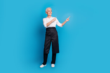 Full size photo of retired female barista coffee shop owner point look empty space wear waitress uniform isolated on blue color background