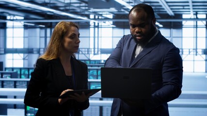 Team of IT specialists managing data center with advanced technology using devices. Coworkers in...