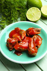 Plate with canned fish in tomato sauce, lime and dill on green wooden table