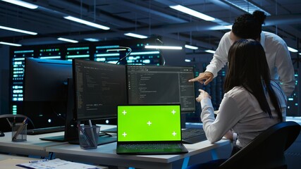 Engineer in high tech data center managing and maintaining databases using mockup devices, ensuring data integrity. Indian employees updating server room supercomputers with chroma key laptop