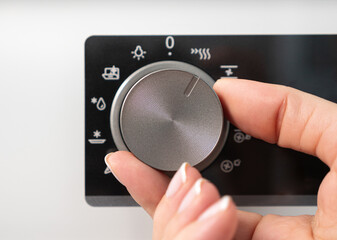 Woman adjusting modern white oven in kitchen.  Female hand pushing and turning knobs on oven control panel