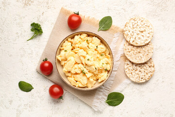 Composition with bowl of scrambled eggs and rice crackers on light background