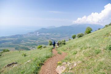 Fototapeta premium Two tourists with backpacks are traveling along a mountain path in summer.