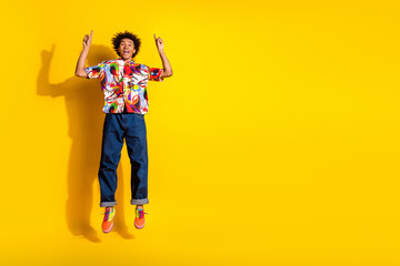 Full size photo of nice funky young man jump direct fingers up empty space wear shirt isolated on bright yellow color background