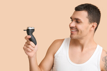 Handsome young man with electric shaver on beige background