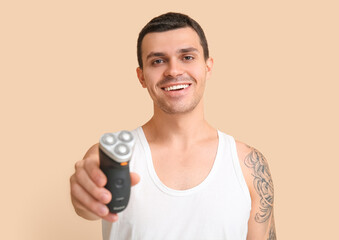 Handsome young man with electric shaver on beige background