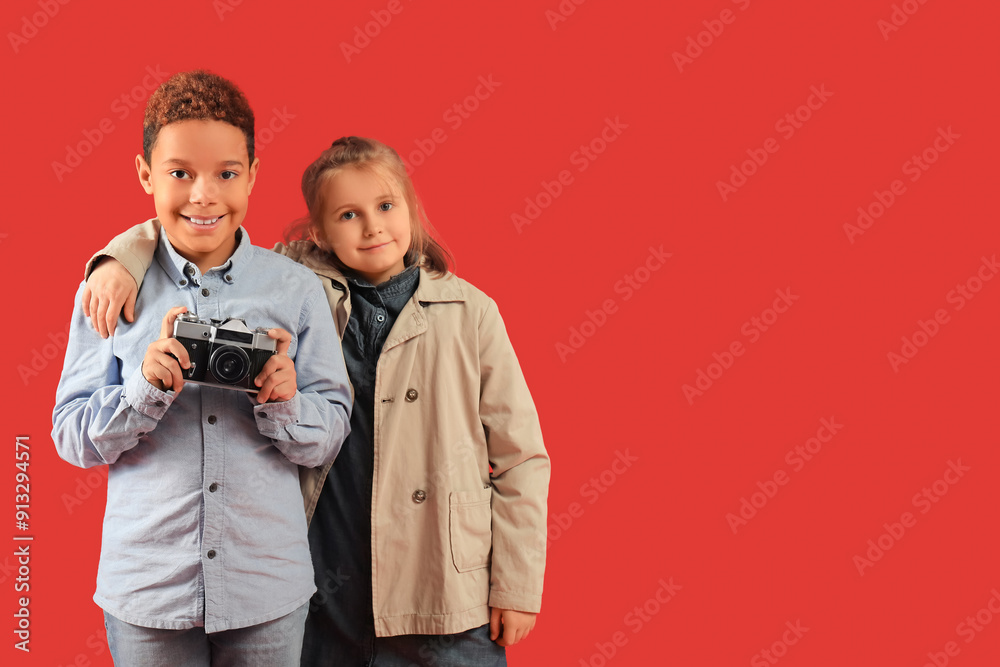 Poster Cute little happy kids in warm clothes with photo camera on red background