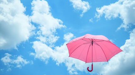 Pink umbrella open under a serene blue sky filled with soft, fluffy clouds, symbolizing protection and beauty.