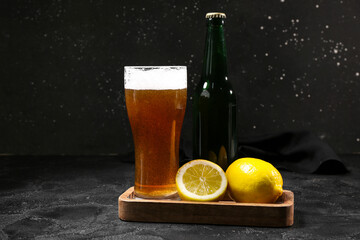 Bottle and glass of fresh beer with lemon on black background