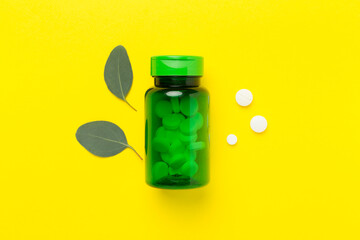 Bottle with pills and green leaves on color background, top view