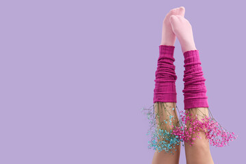 Female legs in gaiters and socks with gypsophila flowers on lilac background