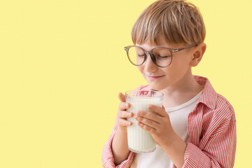 Cute little boy with glass of milk on yellow background