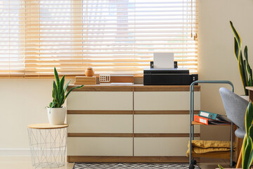 Modern printer with books on commode near window in office