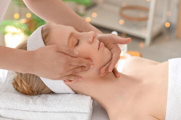 Naklejka premium Young woman having facial massage procedure in spa salon