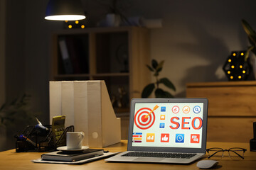 Laptop with abbreviation SEO on desk in dark office