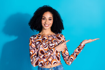 Photo of lovely cheerful woman wearing stylish print clothes presenting empty space isolated on blue color background