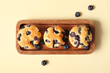 Wooden tray with tasty blueberry muffins on beige background
