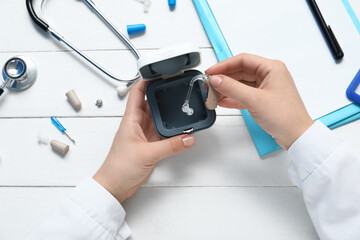 Hands of female doctor with hearing aid, accessories, stethoscope and clipboard on white wooden background, closeup
