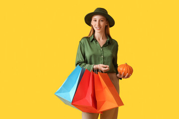 Young woman in autumn clothes with shopping bags and pumpkin on yellow background