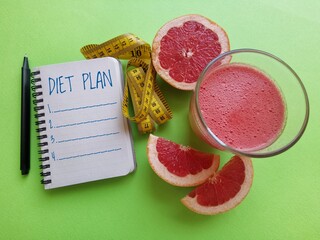 A glass of fresh grapefruit juice, notebook with diet plan, grapefruit slices and measuring tape....