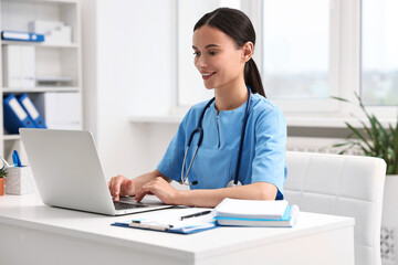 Smiling nurse working with laptop at table in clinic