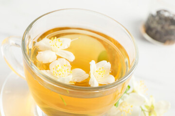 Aromatic jasmine tea in cup and flowers on table, closeup