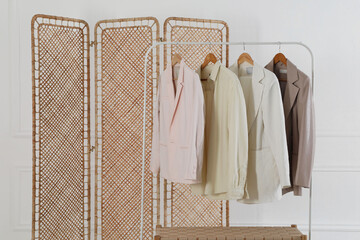 Folding screen, rack with clothes and storage bench near white wall indoors