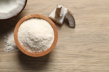 Fresh coconut flour in bowl and nut on wooden table, top view. Space for text