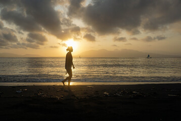Fototapeta premium Silhouette of a woman walking on the beach at sunrise.