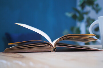 An open book with its pages gently turning rests on a wooden table in the breeze