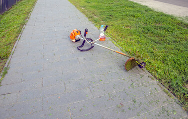 A gas lawn mower is lying on the sidewalk