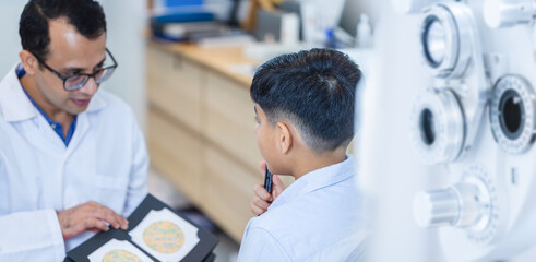 Obraz premium Boy doing eye test checking examination with optometrist in optics store, Indian kid boy choosing eyeglasses in optics store, Optometrist doing color blindness disease perception test in optical shop