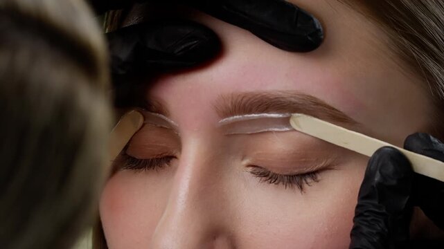 Precision Waxing on Eyebrows. Beauty technician precisely applying wax to the client's eyebrows using a spatula focusing on sanitation and professional beauty standards