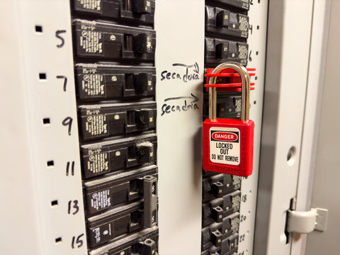 Red padlock for lockout tagout on a breaker inside an electrical panel.