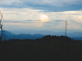 Fototapeta premium Mountains under a cloudy sky at sunset. Lush greenery in the foreground contrasts beautifully with the misty distant mountains. Serene view of Phu Soi Dao National Park in Thailand.