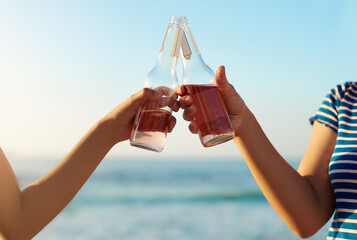 Hands, people and cheers with beer at beach for celebration, summer vacation and bonding together. Friends, women and alcohol toast zoom by ocean for birthday party, outdoor event and holiday travel