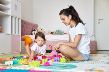 cute little baby girl and her mom playing with colorful blocks in the children room, having fun together