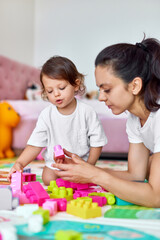 cute baby girl and her loving mother playing with colorful blocks in the children room, early development