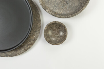 Top view of brown marble tray, black plate and bowl on white background. Food presentation, dishes, stone tray. Copy space, flat lay.