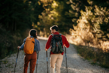 A rear view of a couple with backpacks strolls through the woods, symbolizing the harmony between...