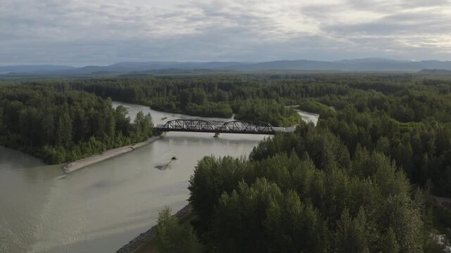 Train traveling over tressel bridge above Susitna River with mountain landscape near Talkeetna, Alaska - 4K Drone