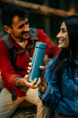 Hiker holding insulated drink container while sitting with boyfriend
