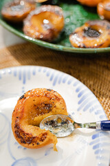 spoon cutting through sticky juicy grilled peach on ceramic plate