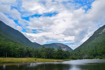 Serene lake surrounded by lush green mountains and a blue sky.