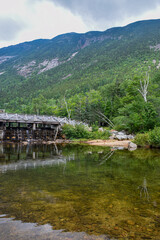 Wooden bridge and dam over a calm river with mountainous backdrop.