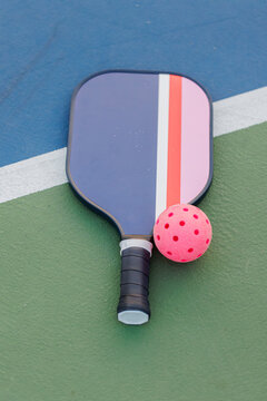 Pickleball paddle and pink ball on green and blue court.