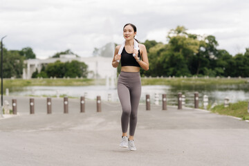 Young woman jogging in the city park Happy brunette female athlete enjoys jogging outdoors. A cute fit woman in a black tracksuit is