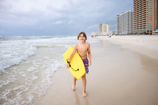 Preteen boy walking on sandy beach carrying boogie board