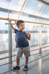 Young boy with backpack standing in modern sunlit airport terminal corridor.